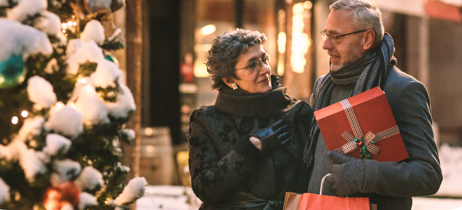 Frau mit Mann beim Weihnachtseinkauf vor einem Geschäft in weihnachtlicher Atmosphäre